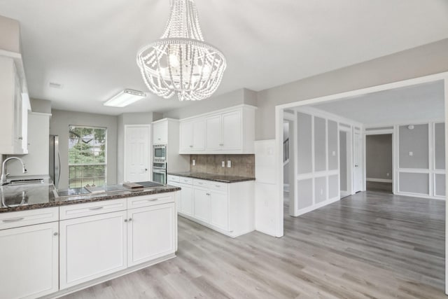 kitchen with pendant lighting, backsplash, white cabinets, a notable chandelier, and stainless steel appliances