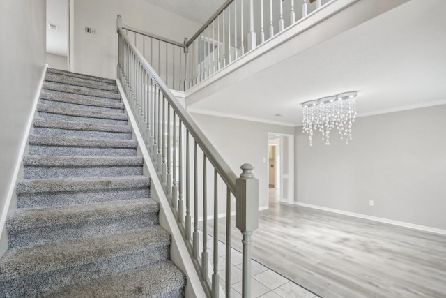 stairs with crown molding, hardwood / wood-style flooring, and an inviting chandelier