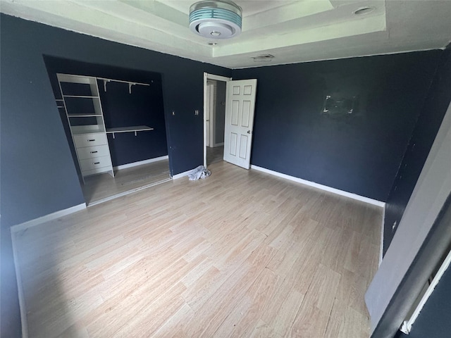 unfurnished bedroom with light hardwood / wood-style floors, a raised ceiling, and a closet