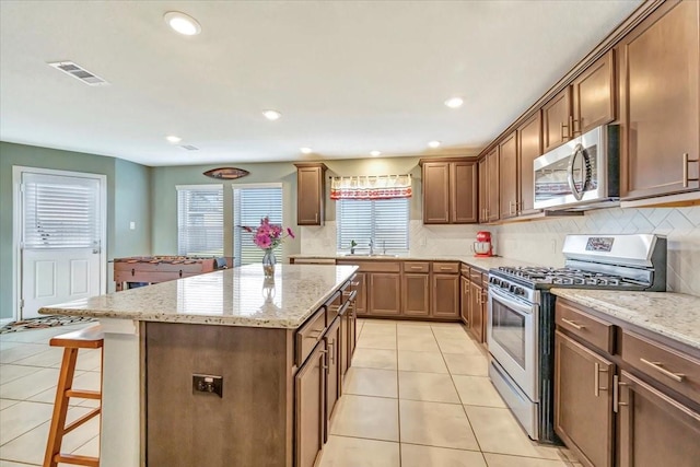 kitchen with a breakfast bar, decorative backsplash, appliances with stainless steel finishes, a kitchen island, and light stone counters