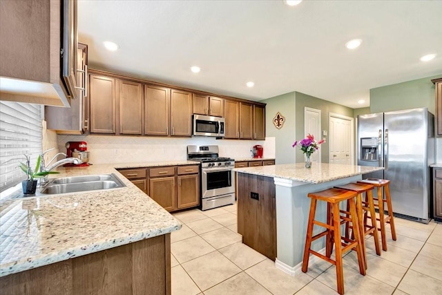 kitchen with a kitchen island, light stone counters, sink, and appliances with stainless steel finishes