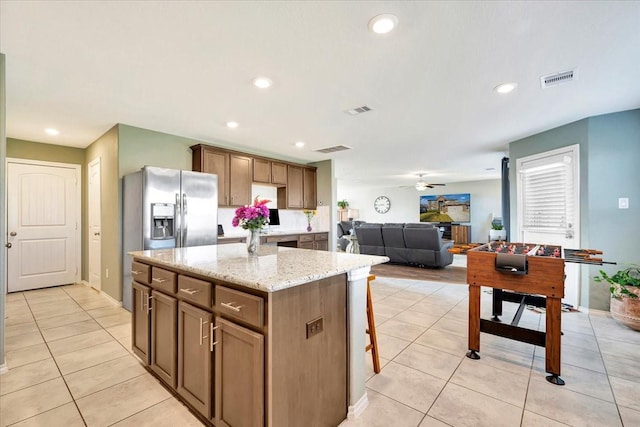 kitchen with a center island, stainless steel refrigerator with ice dispenser, ceiling fan, light tile patterned flooring, and light stone counters