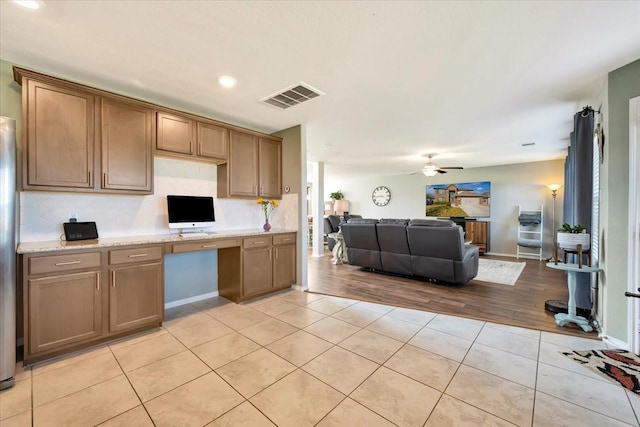 kitchen featuring light stone countertops, light tile patterned floors, built in desk, and ceiling fan