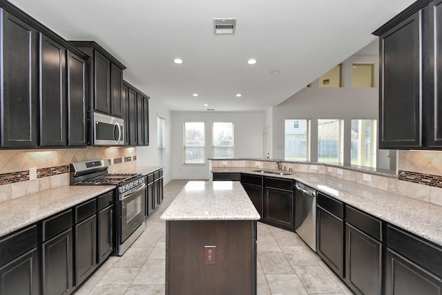 kitchen featuring light stone countertops, a center island, sink, stainless steel appliances, and light tile patterned floors