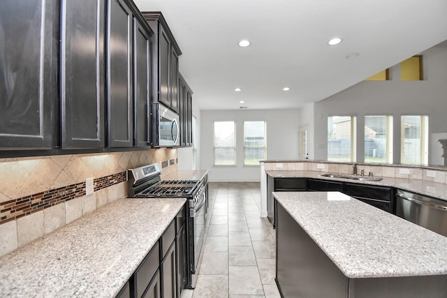 kitchen with backsplash, light stone counters, stainless steel appliances, sink, and a kitchen island