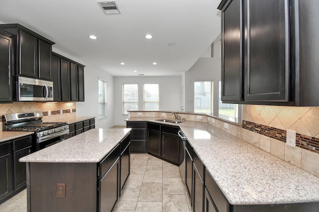 kitchen with light stone countertops, sink, stainless steel appliances, tasteful backsplash, and a kitchen island