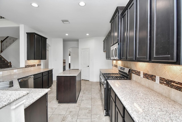 kitchen featuring a center island, sink, tasteful backsplash, light stone counters, and appliances with stainless steel finishes