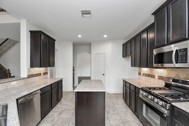 kitchen with light stone countertops, a center island, tasteful backsplash, light tile patterned floors, and appliances with stainless steel finishes