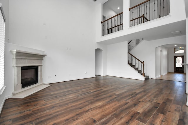 unfurnished living room with a fireplace, a towering ceiling, a wealth of natural light, and dark wood-type flooring