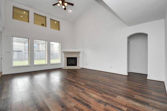 unfurnished living room with ceiling fan, a towering ceiling, and dark wood-type flooring