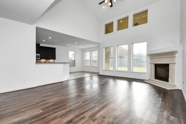 unfurnished living room with ceiling fan, a towering ceiling, and dark wood-type flooring