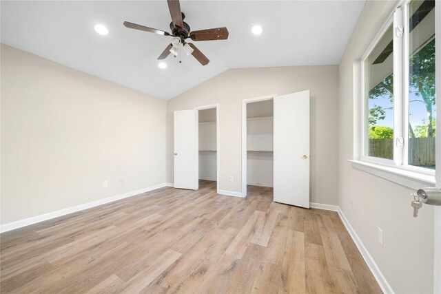 unfurnished bedroom featuring lofted ceiling, a walk in closet, ceiling fan, light hardwood / wood-style floors, and a closet