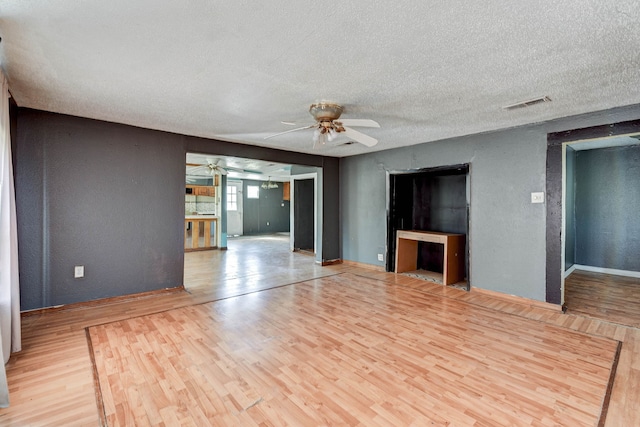 unfurnished living room featuring ceiling fan, light wood-type flooring, and a textured ceiling