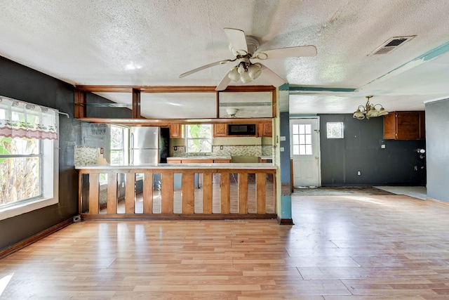 kitchen featuring ceiling fan with notable chandelier, stainless steel fridge, light wood-type flooring, and a textured ceiling