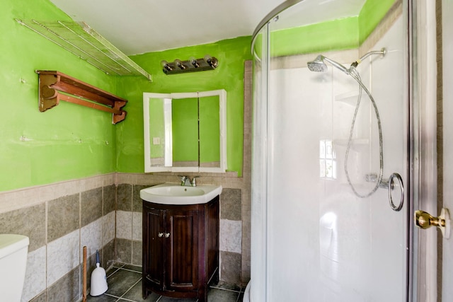 bathroom featuring vanity, a shower with door, tile walls, tile patterned flooring, and toilet