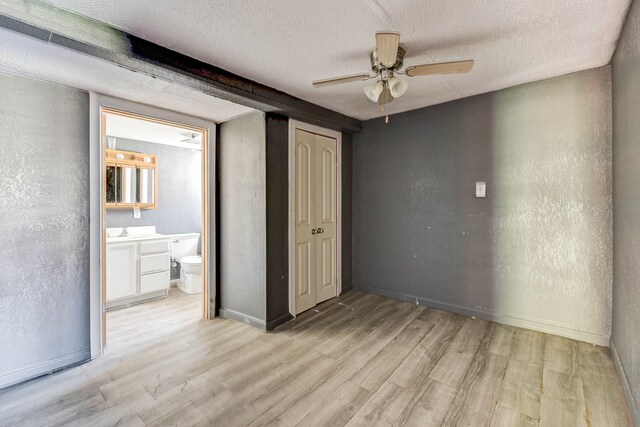 unfurnished bedroom featuring ensuite bathroom, ceiling fan, light wood-type flooring, and a textured ceiling