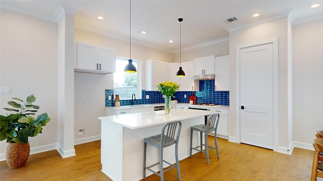 kitchen with crown molding, light hardwood / wood-style flooring, a center island, white cabinetry, and a breakfast bar area