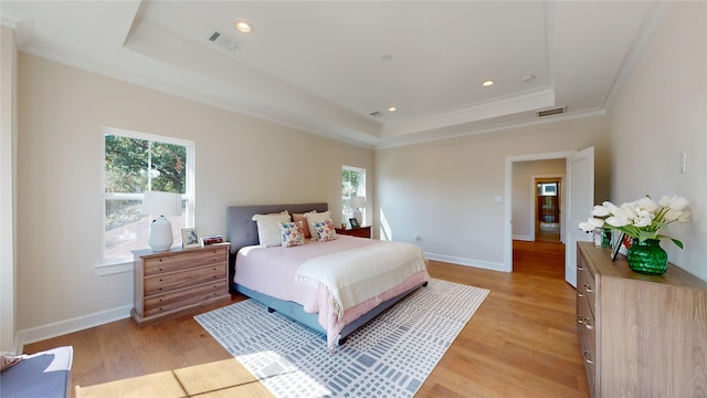 bedroom featuring a tray ceiling, crown molding, and light wood-type flooring