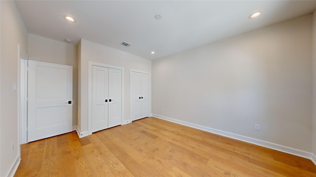 unfurnished bedroom with two closets and light hardwood / wood-style floors