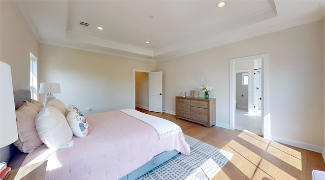 bedroom with light hardwood / wood-style floors, a raised ceiling, and crown molding