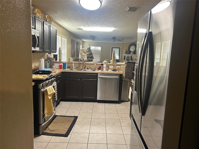 kitchen featuring sink, ceiling fan, light tile patterned floors, a textured ceiling, and stainless steel appliances