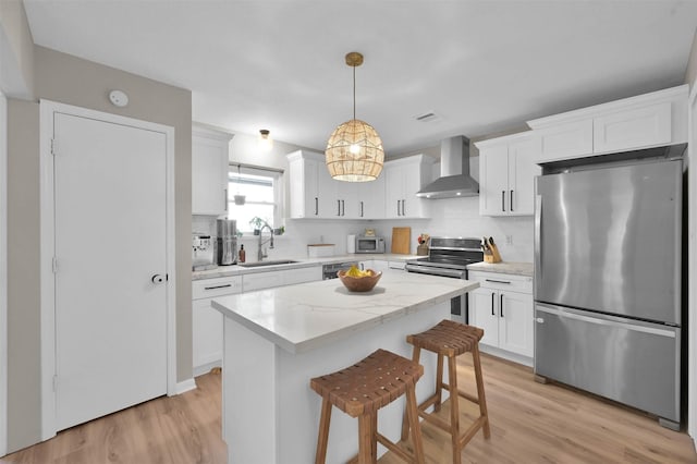 kitchen featuring white cabinetry, stainless steel appliances, wall chimney range hood, decorative light fixtures, and a kitchen island