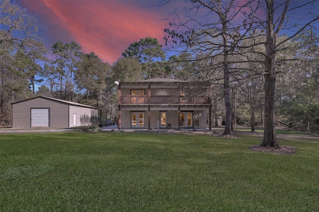 back house at dusk with a yard, a balcony, an outbuilding, and a garage