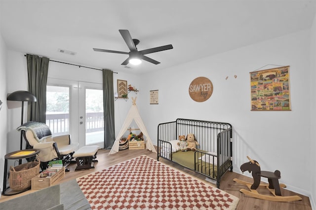 bedroom featuring ceiling fan, french doors, a crib, and hardwood / wood-style flooring