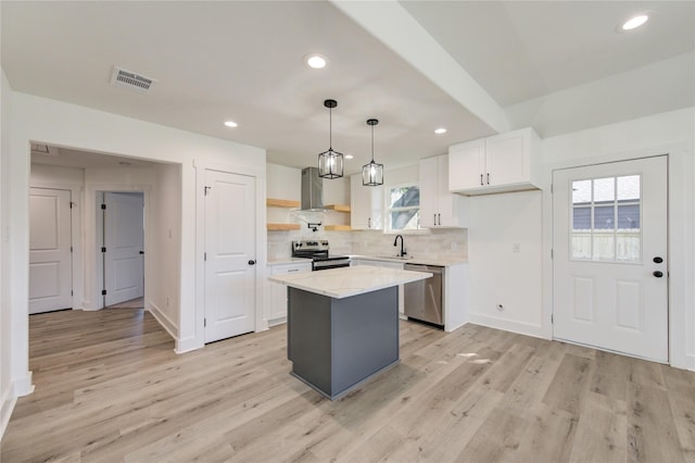 kitchen featuring a center island, wall chimney exhaust hood, decorative light fixtures, white cabinets, and appliances with stainless steel finishes