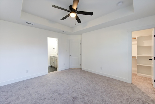 unfurnished bedroom featuring a tray ceiling, a spacious closet, ceiling fan, and ensuite bathroom