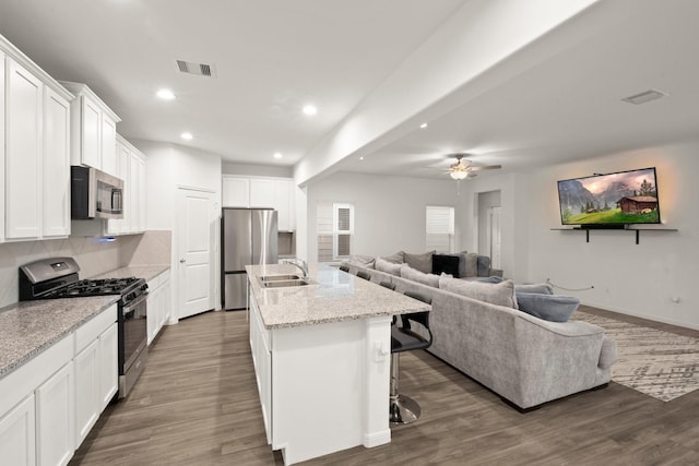 kitchen featuring a kitchen bar, appliances with stainless steel finishes, light stone counters, white cabinetry, and an island with sink