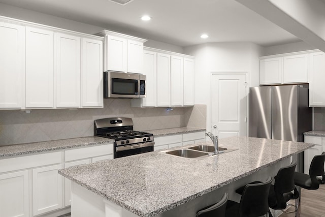 kitchen with decorative backsplash, stainless steel appliances, sink, a center island with sink, and white cabinets