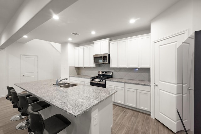 kitchen featuring white cabinetry, sink, light stone counters, an island with sink, and appliances with stainless steel finishes