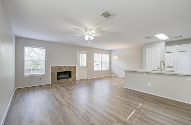 unfurnished living room with a tile fireplace, a wealth of natural light, light hardwood / wood-style flooring, and ceiling fan