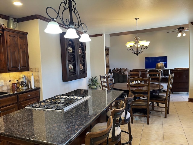 kitchen featuring dark brown cabinetry, stainless steel gas cooktop, dark stone countertops, a breakfast bar area, and light tile patterned flooring