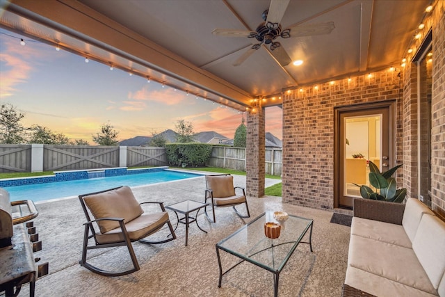 pool at dusk with ceiling fan, an outdoor living space, and a patio