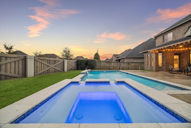 pool at dusk featuring a lawn, a patio area, and an in ground hot tub