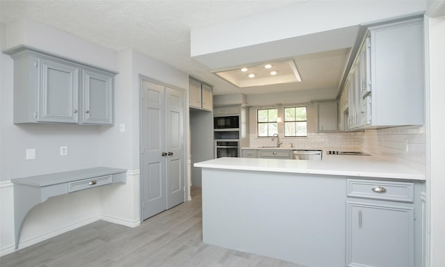 kitchen with kitchen peninsula, backsplash, stainless steel appliances, a tray ceiling, and sink