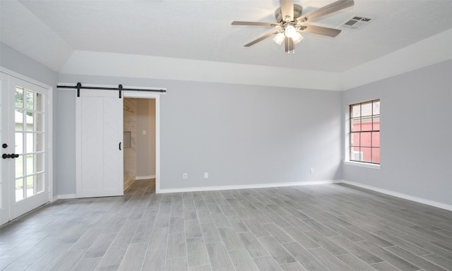 spare room with ceiling fan, a barn door, light hardwood / wood-style flooring, and vaulted ceiling