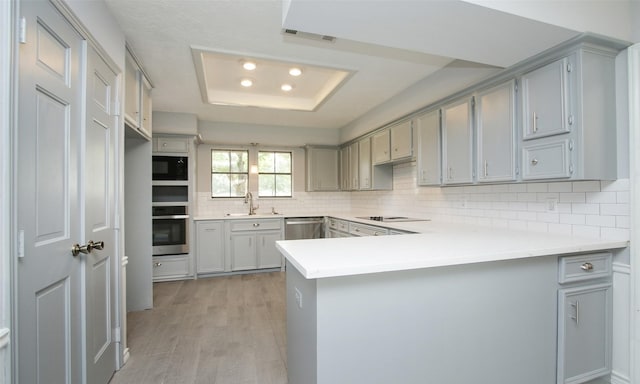 kitchen with gray cabinets, appliances with stainless steel finishes, tasteful backsplash, a tray ceiling, and kitchen peninsula