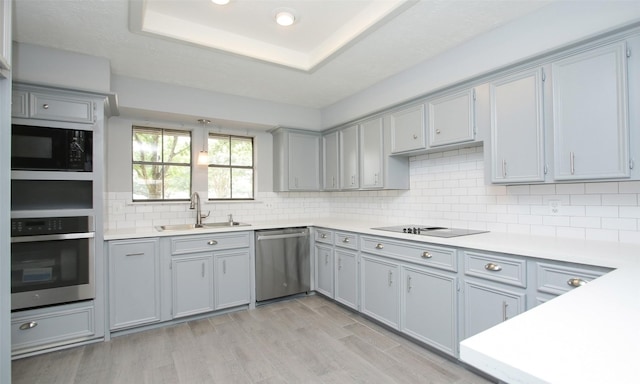 kitchen with decorative backsplash, a tray ceiling, sink, black appliances, and light hardwood / wood-style flooring