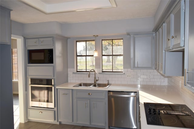 kitchen with gray cabinetry, dark wood-type flooring, black appliances, sink, and decorative backsplash