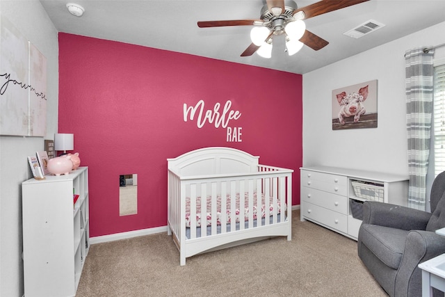 carpeted bedroom featuring ceiling fan and a crib