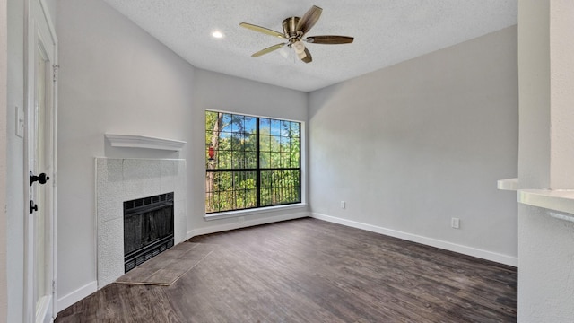 unfurnished living room with a tile fireplace, ceiling fan, dark wood-type flooring, heating unit, and a textured ceiling