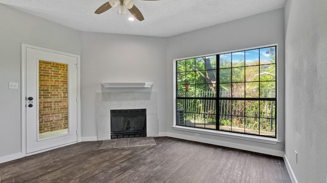 unfurnished living room featuring ceiling fan, a healthy amount of sunlight, dark hardwood / wood-style flooring, and a fireplace