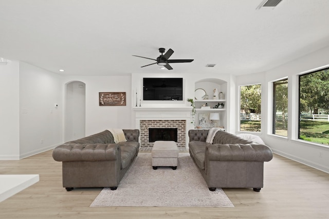 living room featuring ceiling fan, built in shelves, a fireplace, and light hardwood / wood-style flooring