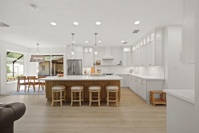 kitchen featuring stainless steel refrigerator with ice dispenser, a kitchen island, custom range hood, pendant lighting, and white cabinets