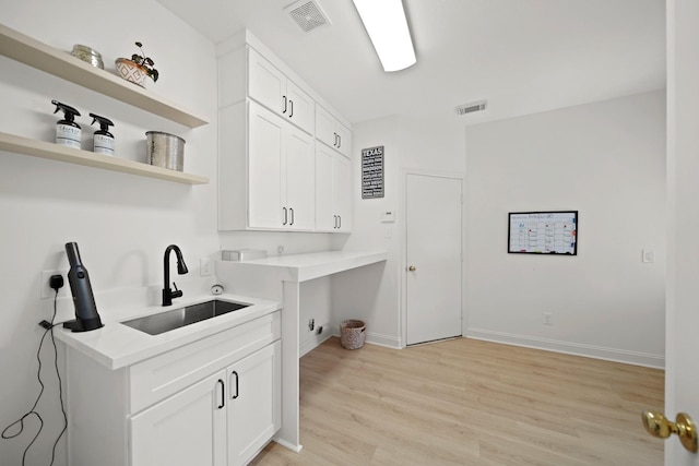 clothes washing area featuring sink, cabinets, and light wood-type flooring