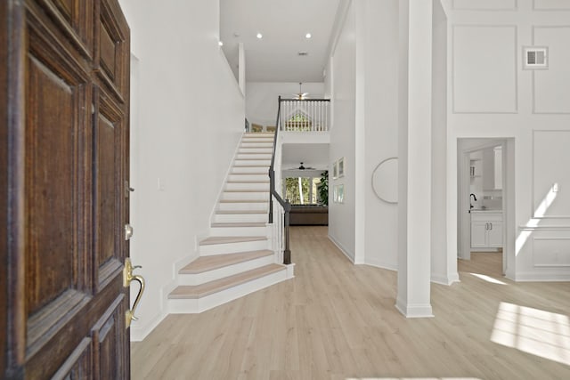 foyer entrance featuring light hardwood / wood-style floors, ceiling fan, and a high ceiling