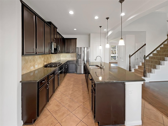 kitchen with stainless steel appliances, a kitchen island with sink, sink, pendant lighting, and light tile patterned floors